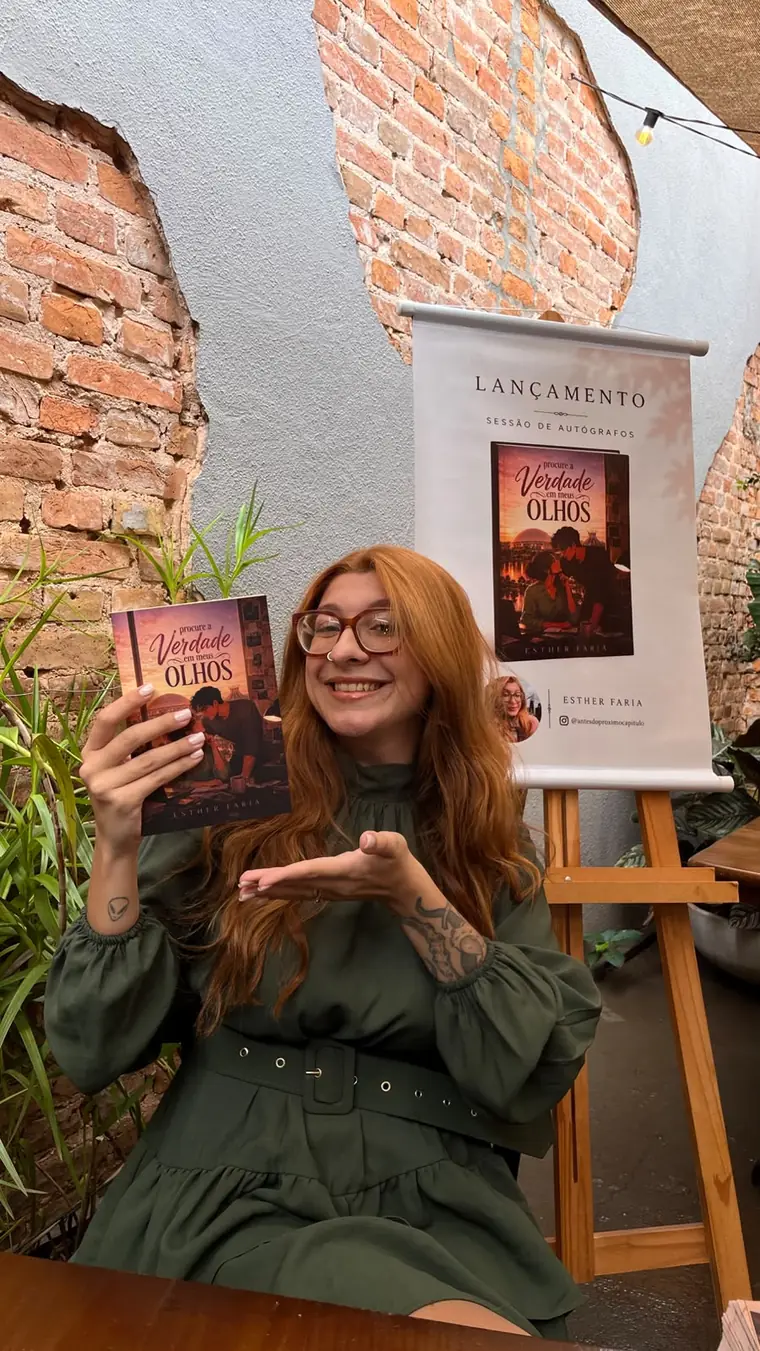 A escritora Esther Faria segurando o livro no lançamento do seu romance de estreia