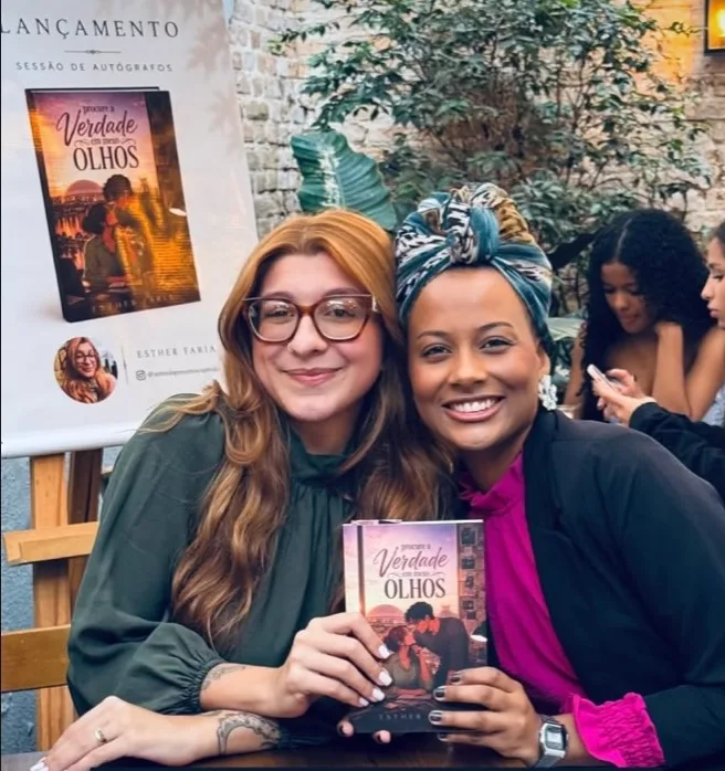 Esther Faria e uma amiga segurando o livro no lançamento